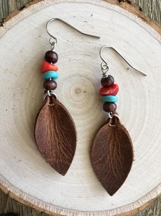 a pair of earrings with leaves and beads hanging from them on a piece of wood