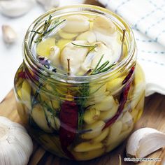 a glass jar filled with pickled vegetables on top of a wooden cutting board next to garlic