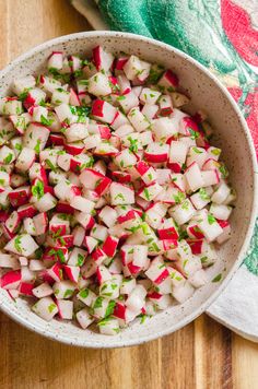 a white bowl filled with chopped radishes on top of a wooden table next to a towel