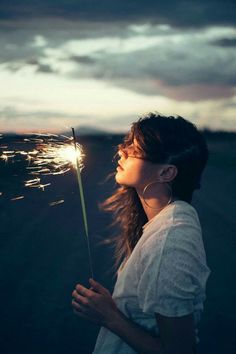 a woman holding a sparkler in her hand and looking at the sky with clouds