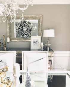 two white chairs sitting next to each other in front of a mirror and chandelier