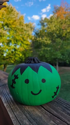 a green pumpkin sitting on top of a wooden table in front of some trees and blue sky