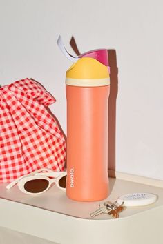 a pink and yellow water bottle sitting on top of a white shelf next to sunglasses