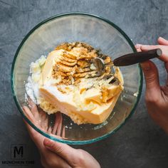 two hands holding a glass bowl filled with dessert and whipped cream, topped with walnuts