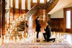 a man kneeling down next to a woman in front of a staircase filled with candles