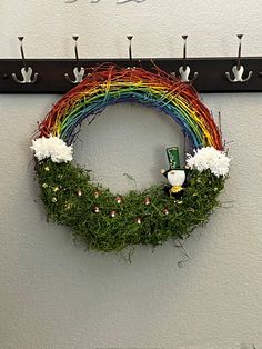 a rainbow wreath is hanging on the wall next to a potted plant and coat rack