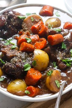 a white bowl filled with stew and carrots on top of a wooden cutting board