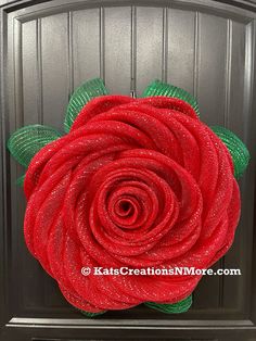 a red rose with green leaves is on the front door and it's made out of mesh