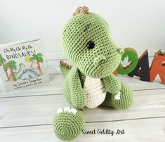 a green crocheted stuffed animal sitting next to a book on a white table