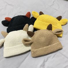 three crocheted hats with horns and ears on top of a white bed sheet