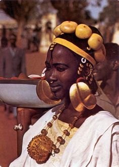 an african woman wearing gold jewelry and holding a bowl