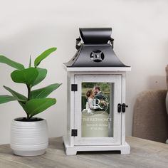 a small white lantern with a photo on it next to a potted plant