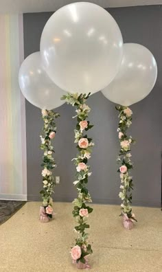 three large white balloons with flowers and greenery on the bottom are standing in front of a gray wall