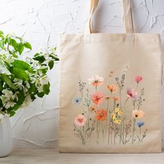 a tote bag with flowers painted on it next to a potted plant and white brick wall