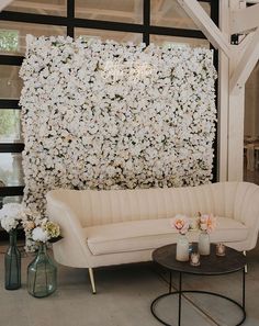 a white couch sitting next to a table with flowers on the wall behind it and candles in vases