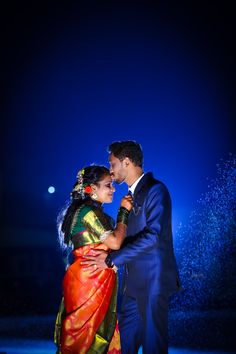 a man and woman are dancing together in the rain at their wedding reception with blue lights behind them