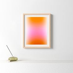 an orange and pink painting hangs on the wall next to a green vase with a yellow flower in it