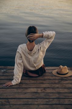 a woman sitting on a dock next to the water covering her face with her hands