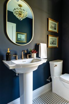 a white toilet sitting next to a bathroom sink under a round mirror on a wall