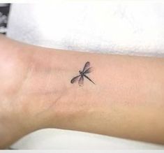 a small dragonfly tattoo on the left inner arm and wrist, sitting on a woman's right leg