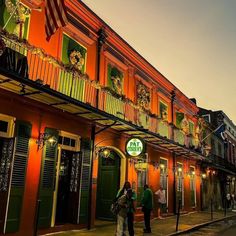 people are walking on the sidewalk in front of an orange building with green shutters