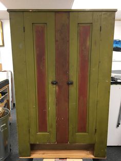 an old green cabinet with red doors in a room next to a trash can and other items