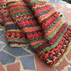 multicolored crocheted gloves sitting on top of a stone floor next to a plant