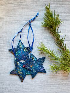 two blue stars hanging from a tree branch on top of a wooden table next to a sprig of pine