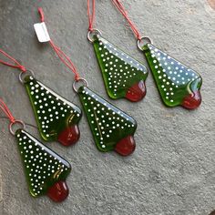 four green and red glass ornaments with white polka dots hanging from strings on a stone surface