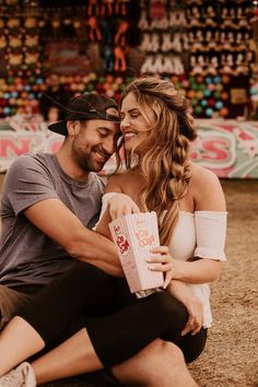 a man and woman sitting next to each other on the ground with popcorn in their hands