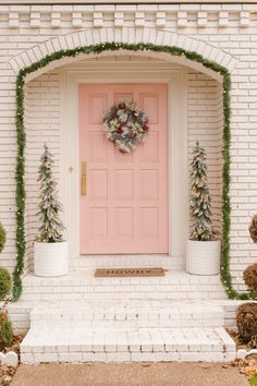 a pink front door with wreaths and potted trees