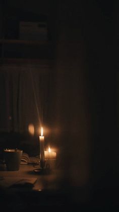 two candles are lit on a table in the dark, with books and cups nearby