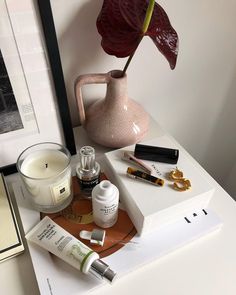 an assortment of beauty products on a table next to a candle and some framed pictures