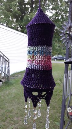 a purple crocheted wind chime hanging from a metal pole in the grass