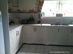 a kitchen with white cabinets and tile flooring next to a window in the corner