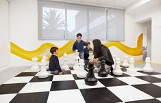 two children and an adult playing chess on a checkered floor