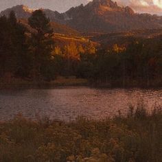 a lake surrounded by trees and mountains under a cloudy sky