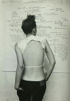 a woman standing in front of a white wall with writing all over it and her back to the camera