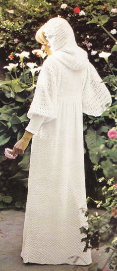 a woman in a white dress is walking through some flowers and bushes with a bird on her hand