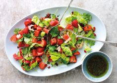 a salad with strawberries and lettuce on a white plate next to a small bowl of dressing