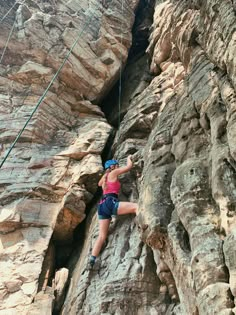 a woman climbing up the side of a mountain with her hands in the air and holding on to ropes