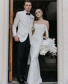 a man and woman standing in front of a doorway holding bouquets with white flowers