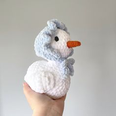 a small crocheted white duck with a carrot in its beak sitting on someone's hand