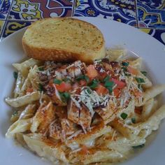 a white plate topped with pasta covered in sauce and cheese next to a slice of bread