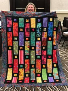 a woman is holding up a colorful quilt