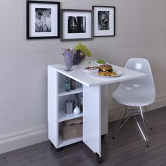 a small table with food on it in front of three framed pictures and a white chair