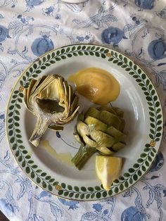 a plate with artichokes and sauce on it sitting on a tablecloth