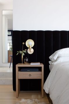 a bedroom with a black headboard, white sheets and a wooden table next to the bed