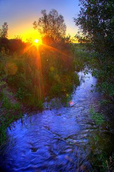 the sun is setting over a small river