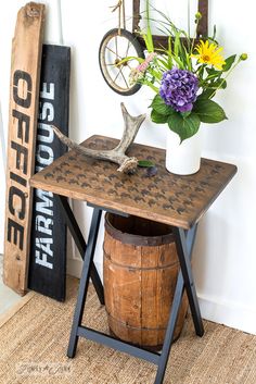 a wooden table topped with a vase filled with flowers next to a wall mounted sign